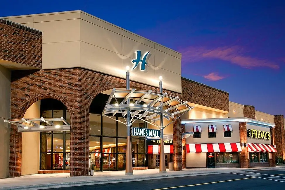 Hanes Mall area in Winston-Salem featuring the mall entrance and nearby restaurants illuminated at dusk, highlighting a popular retail and dining destination.